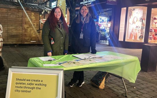 Manchester City Council representatives on a stall on King Street. The sign reads "Should we create a quieter, safer walking route through the city centre?"