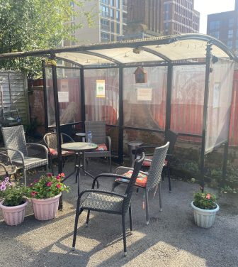 Outdoor area with potted plants, chairs, a table and a smokers' shelter