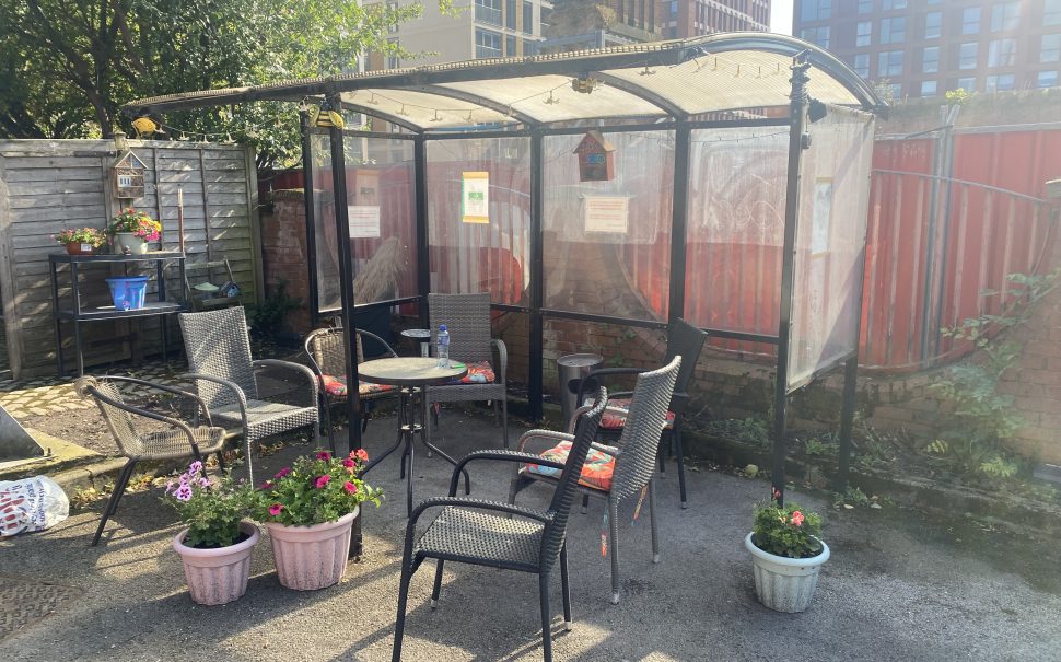 Outdoor area with potted plants, chairs, a table and a smokers' shelter