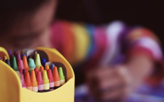 Crayons beside child colouring, by Aaron Burden on Unsplash, Free to use under the Unsplash Licence