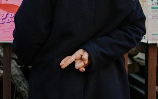 Woman with fingers crossed behind her back, wearing a black coat.